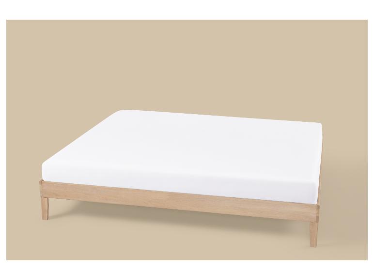 Cadre de lit en bois avec un matelas blanc sur fond marron clair.