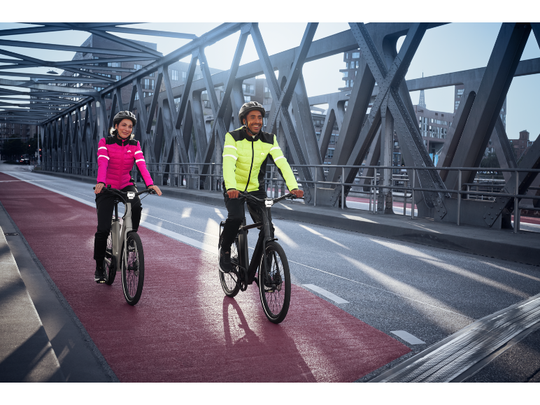 Deux personnes en vestes de cyclisme réfléchissantes et casques à vélo électrique sur un pont.