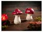 Deux champignons décoratifs en céramique rouge à pois blancs sur une table en bois.