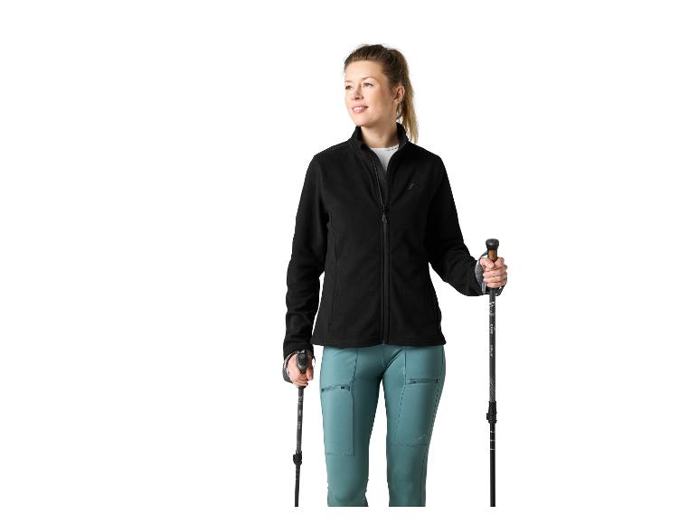 Femme en veste polaire noire et pantalon turquoise, tenant des bâtons de randonnée.