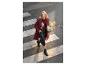 Femme souriante en manteau bordeaux et jupe en cuir, traversant un passage piéton avec un bouquet de lys.