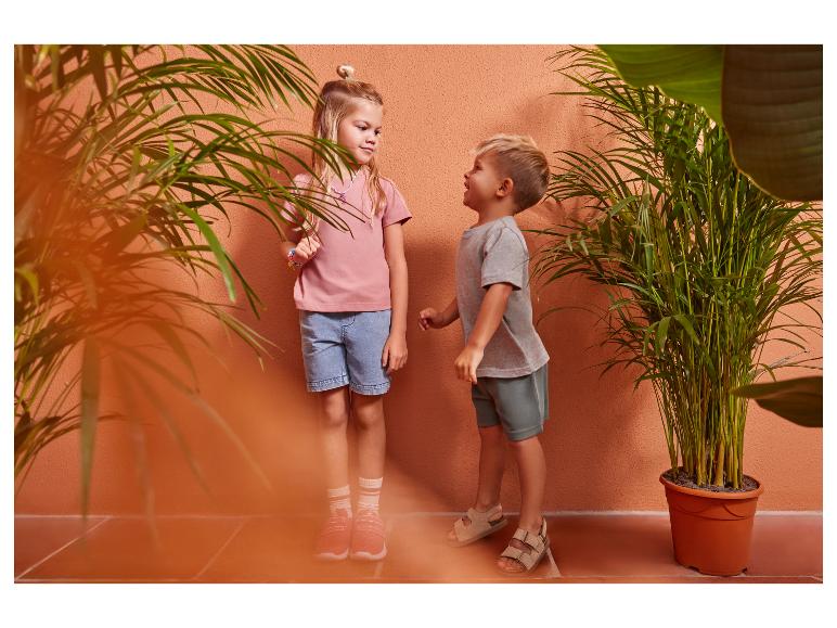 Deux enfants en vêtements d'été décontractés, une fille en t-shirt rose et short en jean, un garçon en t-shirt gris et short vert.