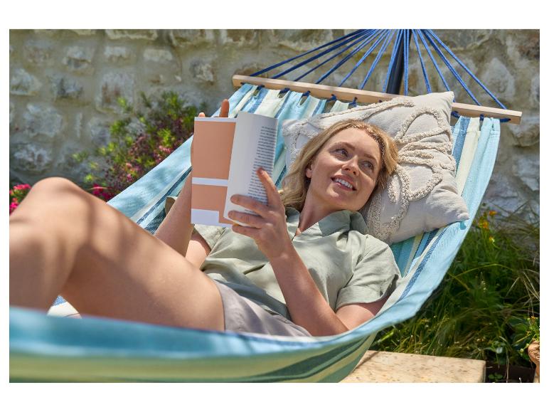 Femme se relaxant dans un hamac avec un livre dans un jardin.