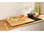 Comptoir de cuisine avec grande planche à découper en bambou, plaque à induction, casserole et légumes frais.