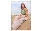 Femme en top vert et pantalon beige assise sur une dune de sable.