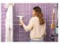 Une femme utilise un nettoyeur de vitres électrique dans une salle de bain aux murs violets.