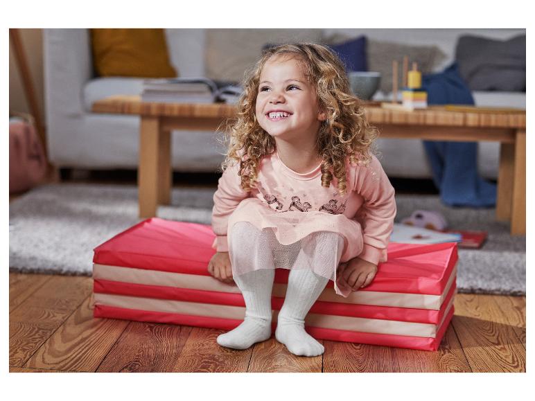 Une petite fille avec une robe rose assise sur un tapis de jeu rose.