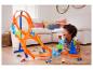 Un garçon joue avec une piste de voitures Hot Wheels, avec des boucles et des rampes, dans le salon.