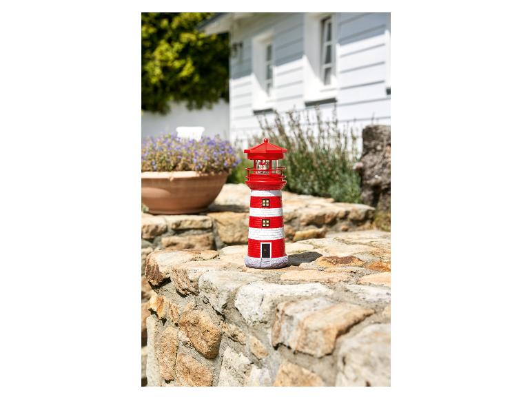 Un phare rouge et blanc avec une lampe, sur un mur de pierre dans le jardin.
