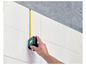 Une main utilise un mètre ruban et un mètre laser Parkside pour mesurer un mur.