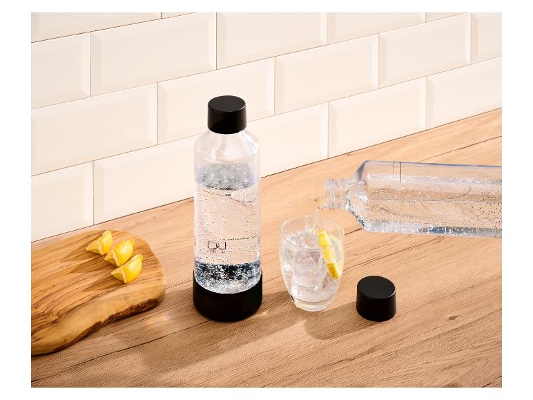 Bouteille d'eau pétillante et verre avec des glaçons et du citron sur un comptoir en bois.