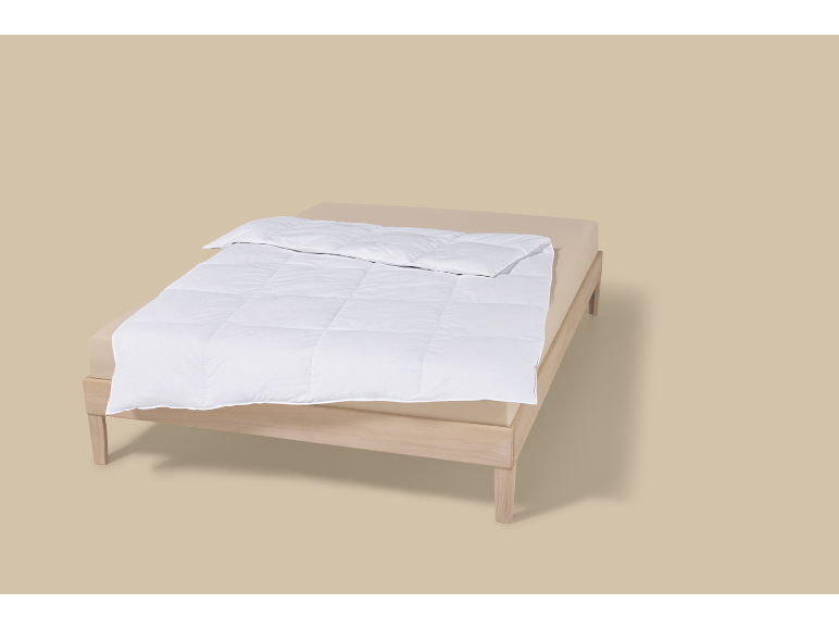 Un lit avec une couette blanche et un drap-housse beige clair.