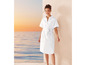 Une femme en robe blanche devant un coucher de soleil sur la mer.