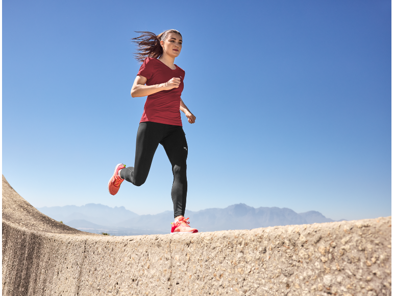 Femme courant en extérieur avec un t-shirt rouge et un legging noir, des chaussures de course orange.