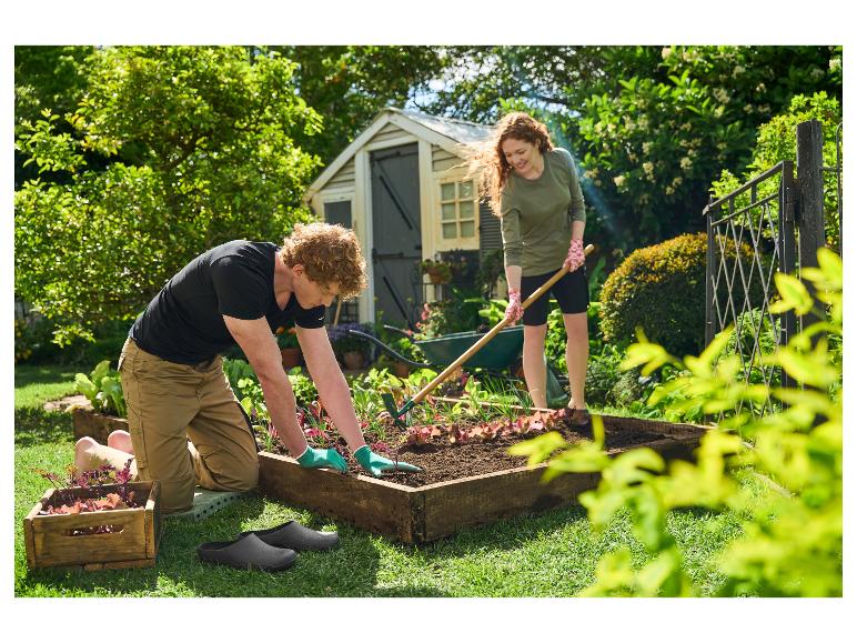 Homme et femme plantant des légumes dans un potager surélevé, avec des sabots de jardin et des outils.