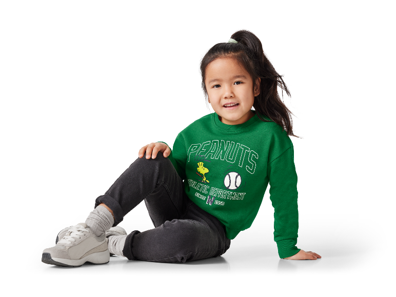 Petite fille portant un sweat-shirt vert Peanuts et des baskets grises.