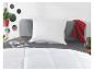 Chambre avec oreiller blanc, couette, linge de lit gris et plaid rouge.