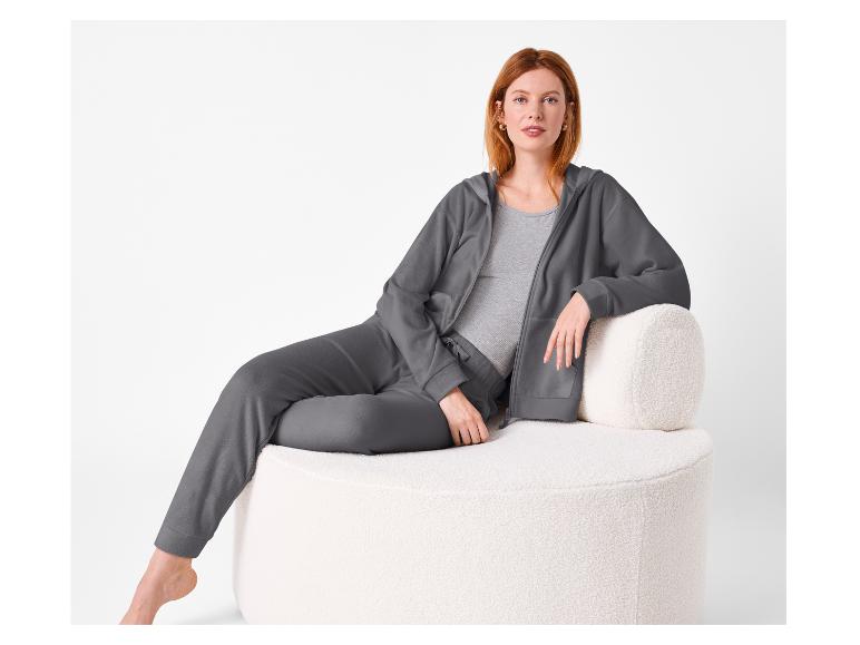 Femme en ensemble de loungewear gris assise sur une chaise blanche texturée.