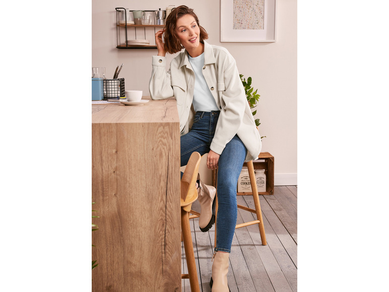 Une femme porte un t-shirt bleu clair, une veste blanche et un jean skinny bleu.