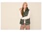 Femme en gilet matelassé vert, pull beige, pantalon marron et bonnet beige.