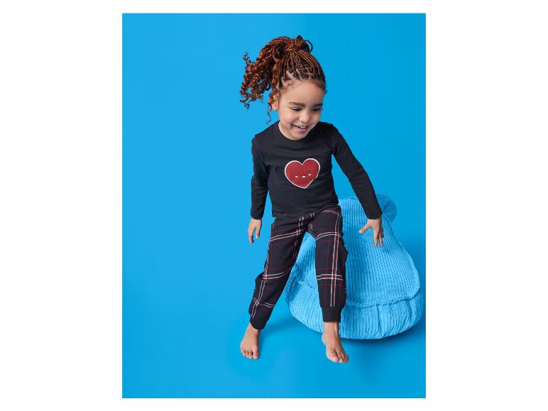 Fille souriante en pyjama noir avec un cœur rouge, debout sur un coussin bleu.