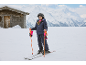Fille en veste de ski, pantalon de ski, casque et gants de ski sur une piste enneigée.