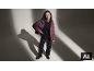 Une femme en doudoune mauve, pull noir et pantalon noir posant dans un studio.