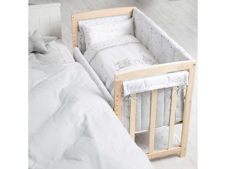 Un lit bébé en bois avec un motif d'étoiles et un doudou étoile gris.