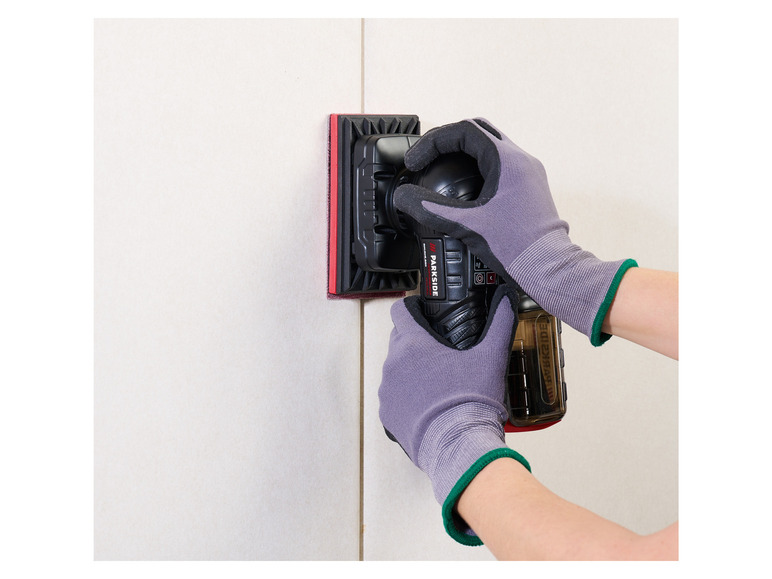 Une personne utilise une ponceuse Parkside sur un mur de carreaux.