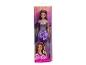Une poupée Barbie en robe violette et collier argenté, dans son emballage.