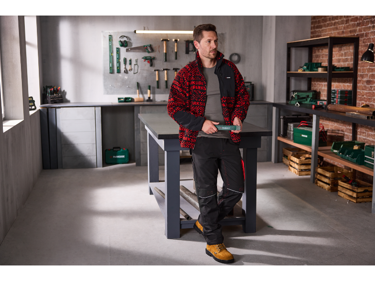 Homme en veste polaire rouge et noire et pantalon de travail dans un atelier.