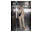 Femme souriante en survêtement beige et sac banane noir dans un ascenseur en métal.