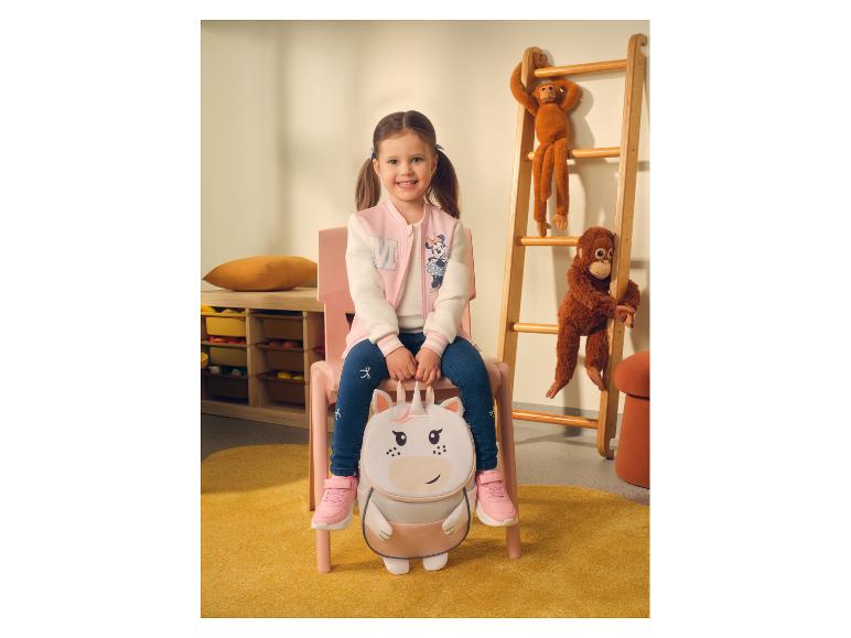Fille en veste de baseball et jean, assise sur une chaise avec un sac à dos licorne.
