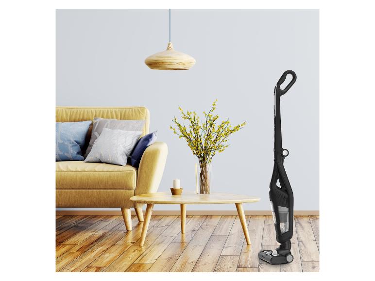 Aspirateur balai noir dans un salon moderne avec canapé jaune et table basse en bois.