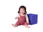 Bébé heureux en barboteuse tricotée rose assis à côté d'un cube bleu.