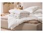 Piles de couettes et oreillers blancs sur un lit beige.