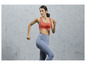 Une femme en soutien-gorge de sport rose et leggings bleus en train de courir.