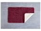 Tapis de bain bordeaux sur un sol gris.