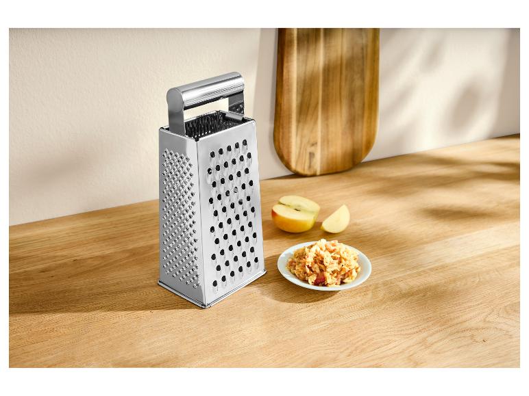 Râpe à quatre faces en acier inoxydable avec des pommes râpées sur un comptoir en bois.