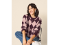 Femme souriante en pull à losanges violets et jean, assise sur une chaise.
