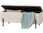 Banc de rangement blanc en tissu teddy avec un coussin beige et une couverture tricotée bleu clair.