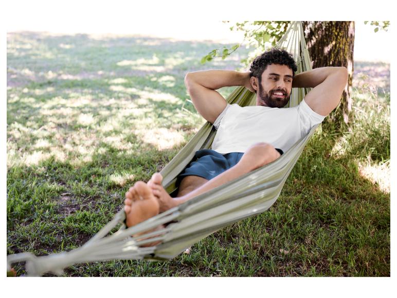 Homme en t-shirt blanc et short se relaxant dans un hamac en extérieur.