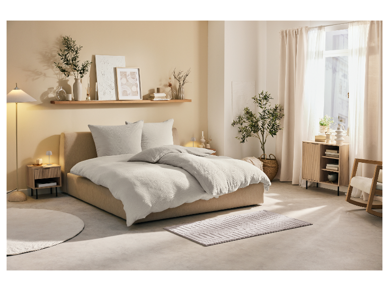 Lit avec linge de lit en coton bio et meubles en bois clair dans une chambre minimaliste.