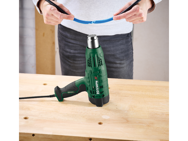 Pistolet thermique vert sur un établi en bois, avec une personne tenant un câble bleu.