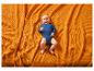 Adorables bébé en body bleu, allongé sur une couverture orange texturée.