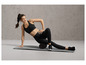Une femme en tenue de sport utilise un rouleau en mousse sur un tapis de yoga.
