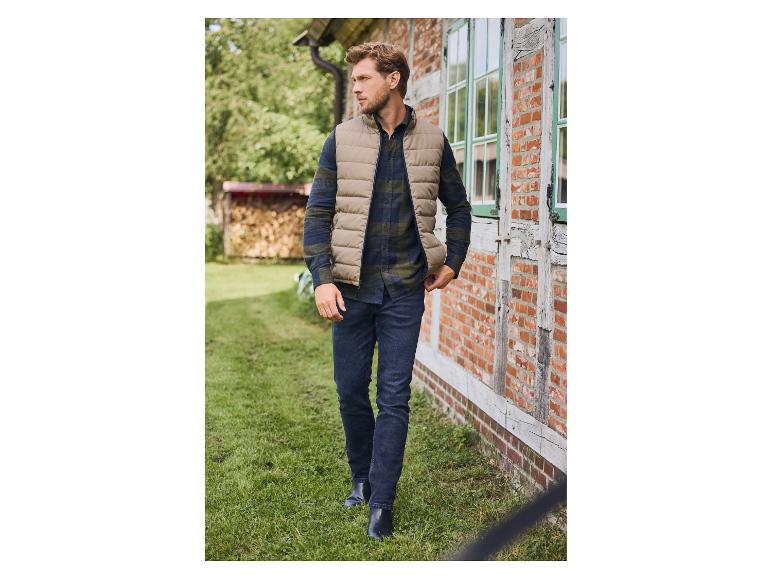 Homme en gilet matelassé beige, chemise à carreaux et jean marchant à l'extérieur.