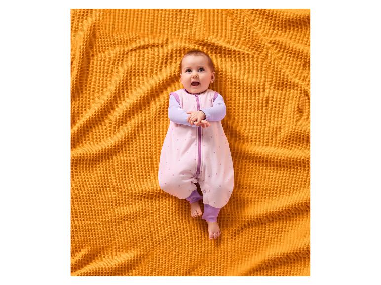 Bébé souriant dans une gigoteuse rose à étoiles, allongé sur une couverture orange.