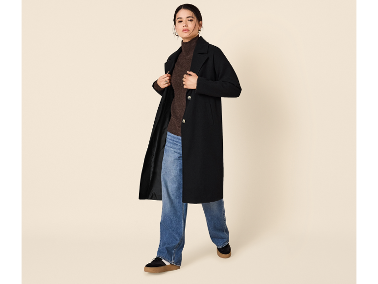 Femme en manteau noir, pull marron et jean.