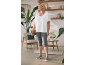 Femme en T-shirt blanc et legging capri gris, tenant un sac tressé, dans une pièce chaleureuse.